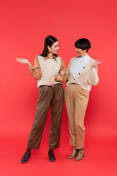 Full length of happy asian mother and daughter looking at each other on coral background — Stock Photo
