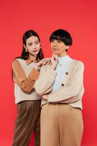 Young asian woman leaning on shoulder of brunette mother isolated on coral — Stock Photo