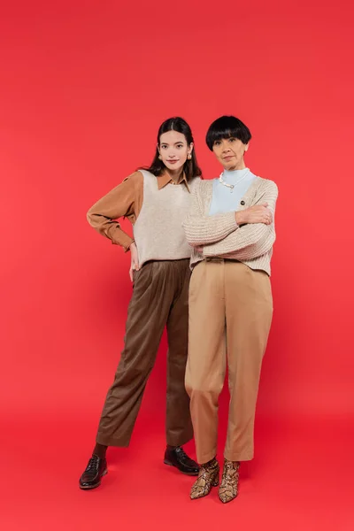 Full length of stylish asian mother and daughter in trendy clothes posing on coral background — Stock Photo