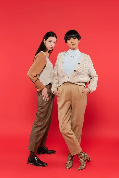 Full length of asian mother and daughter in trendy clothes posing on coral background — Stock Photo