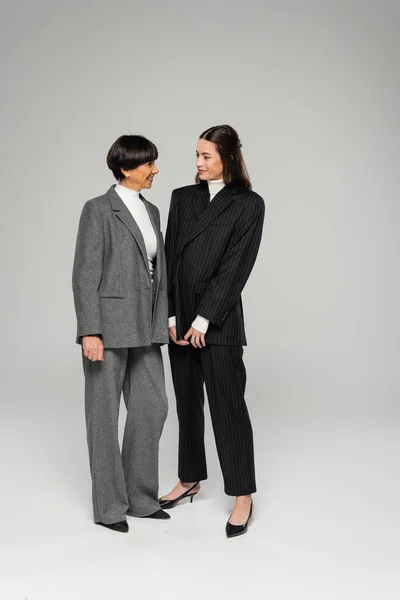 Volle Länge der fröhlichen asiatischen Mutter und Tochter in Strumpfhosen schauen einander auf grau — Stockfoto