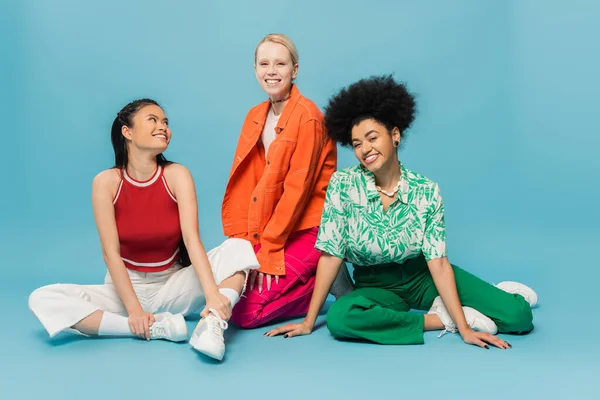 Full length of cheerful multiethnic women in stylish casual attire posing on blue background — Fotografia de Stock