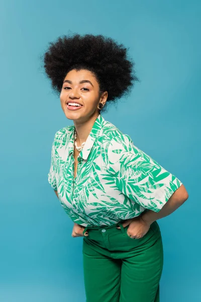 Trendy african american woman in leaf print blouse smiling at camera isolated on blue — Stock Photo