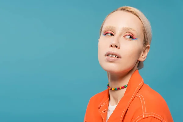 Portrait of pretty blonde woman in colorful beads and bright orange jacket looking away isolated on blue — Foto stock