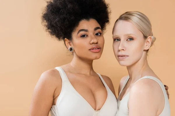 Pretty multiethnic women in underwear looking at camera isolated on beige — Stockfoto