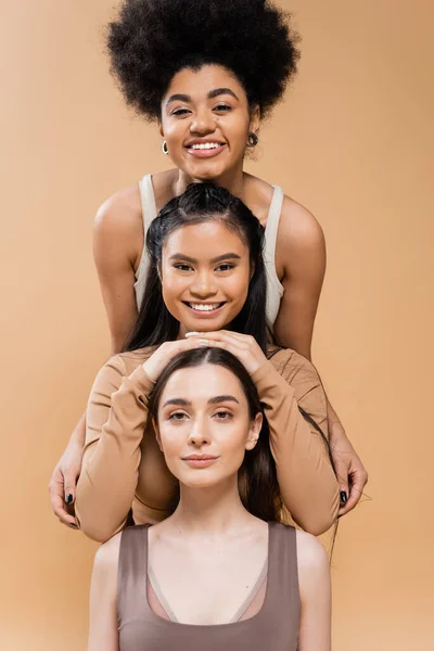 Cheerful multicultural women in lingerie smiling at camera while posing isolated on beige — Stock Photo