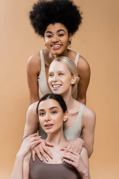 Jolis et joyeux modèles multiethniques en lingerie posant et souriant isolé sur beige — Photo de stock