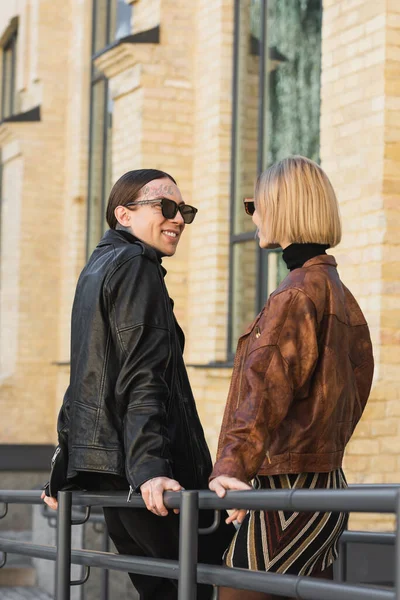 Счастливая пара в стильных солнцезащитных очках и кожаных куртках, улыбающихся, глядя друг на друга — стоковое фото