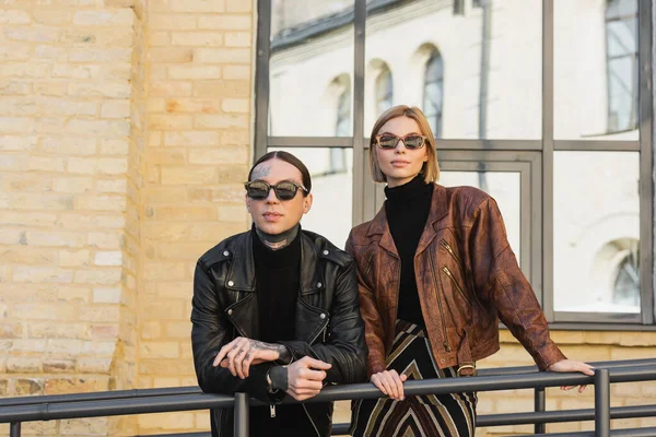 Stylish couple in trendy sunglasses and leather jackets standing outdoors — Photo de stock
