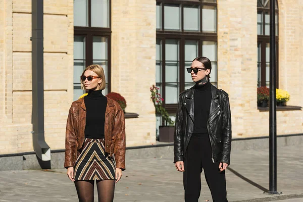 Стильна молода пара в шкіряних куртках і сонцезахисних окулярах, що стоять на міській вулиці — стокове фото