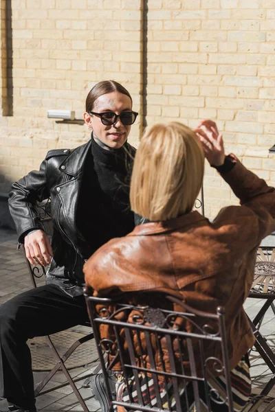 Tattooed man in stylish sunglasses looking at blonde girlfriend in leather jackets — Stock Photo