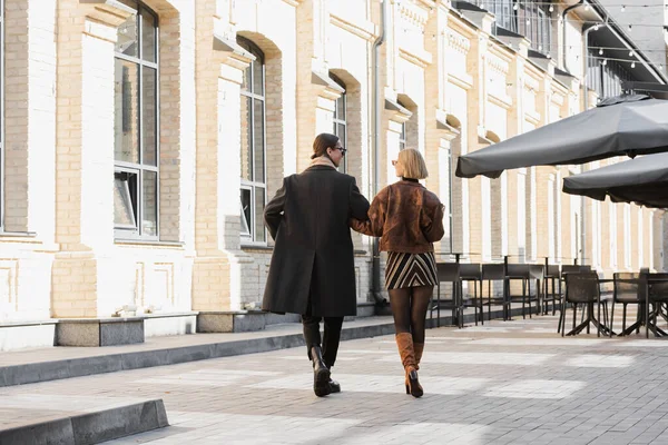 Full length of blonde woman in trendy leather jacket walking with boyfriend on street — Foto stock
