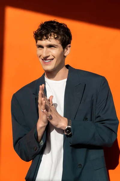 Cheerful and stylish man in jacket posing on orange background with sunlight — Stock Photo