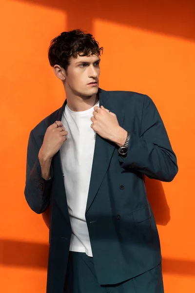 Uomo alla moda in giacca e t-shirt guardando altrove su sfondo arancione — Foto stock