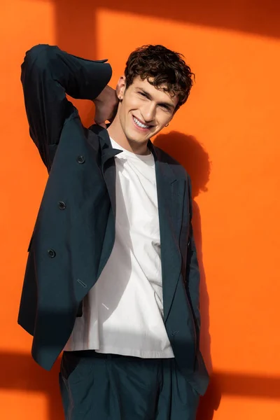 Fröhlicher junger Mann im eleganten Anzug, der den Hals auf orangefarbenem Hintergrund berührt — Stockfoto