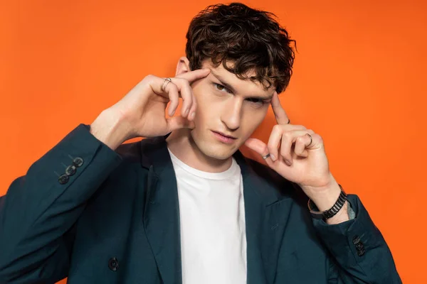 Man in blue jacket touching eyebrows on orange background - foto de stock