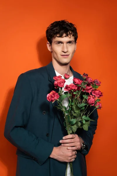 Portrait of smiling man in blue jacket holding roses on red background — Foto stock