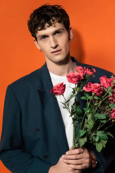 Portrait of man in jacket and t-shirt holding roses on orange background — Photo de stock
