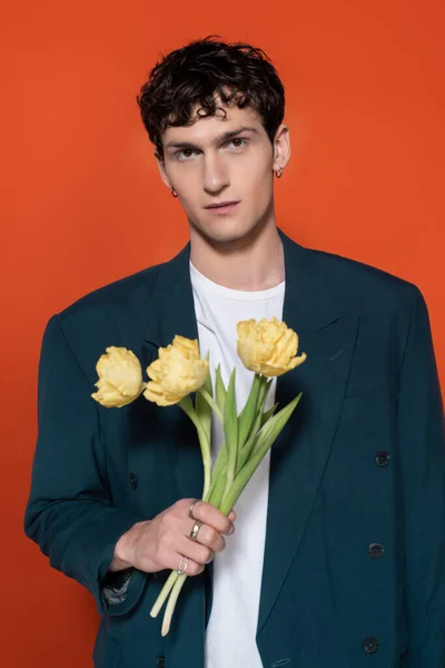 Portrait of stylish brunette man holding yellow tulips isolated on red — Stock Photo