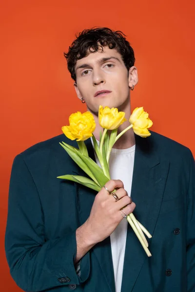 Stylish young model in jacket holding yellow tulip flowers isolated on red — Foto stock