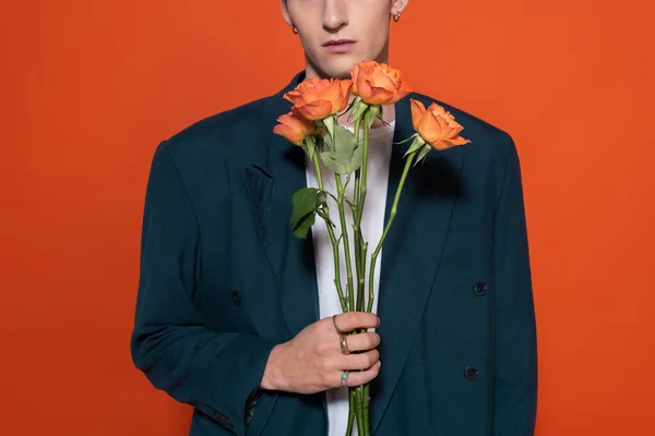 Cropped view of trendy model holding orange roses for 8 march isolated on red — Stock Photo