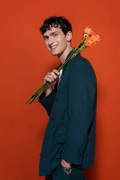 Homem sorridente de terno azul segurando flores de laranja para 8 de março no fundo vermelho — Fotografia de Stock
