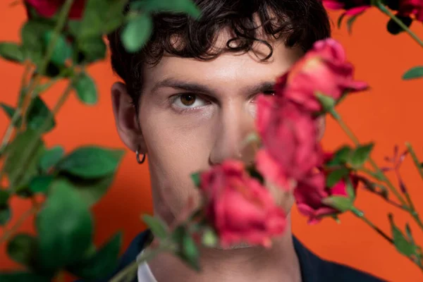 Portrait of curly model looking at camera near blurred flowers on red background — Stock Photo