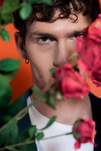 Portrait de jeune homme regardant la caméra près de roses floues sur fond orange — Photo de stock