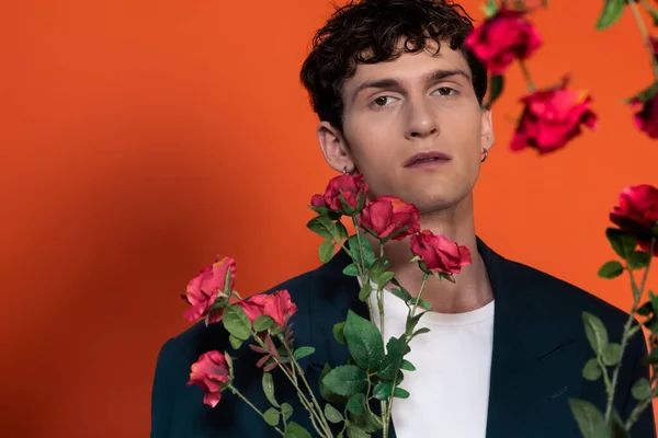 Young man in jacket looking at camera near blurred flowers on red background — Foto stock