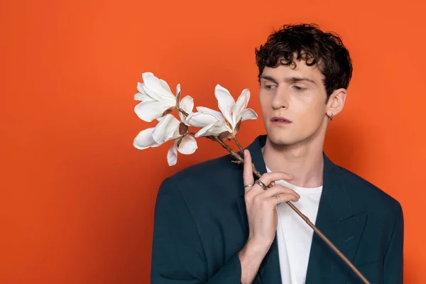 Stylish brunette man looking at magnolia flowers on orange background — Stock Photo