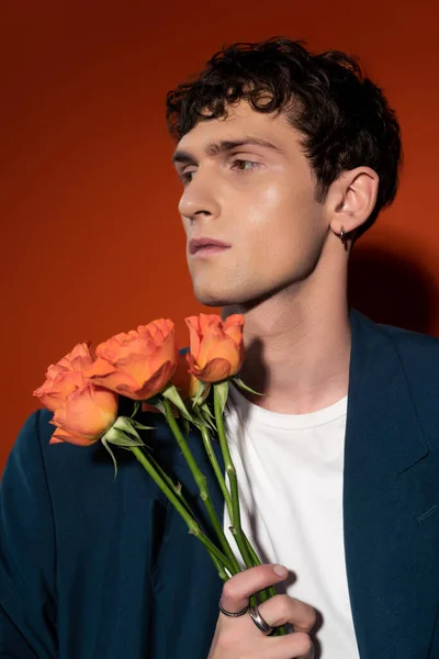 Портрет стильного молодого чоловіка, що тримає помаранчеві троянди на червоному тлі — стокове фото