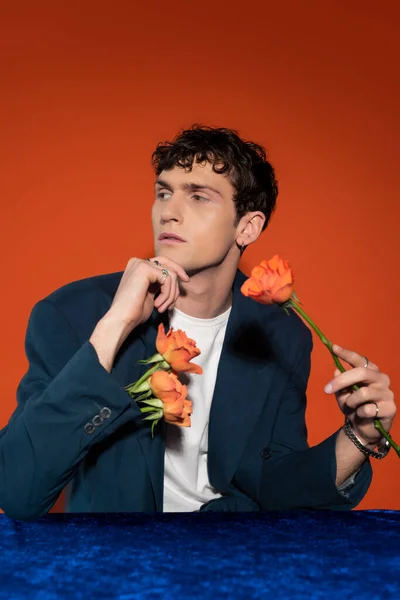Fashionable model in blazer holding with orange flowers on red background - foto de stock