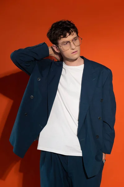 Stylish model in eyeglasses and blue suit posing on red background — Stock Photo