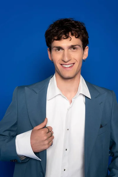 Portrait of smiling and curly model in blazer looking at camera on blue background — Stock Photo