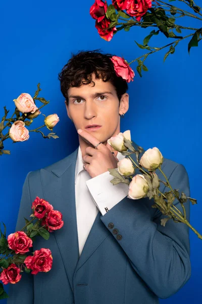 Stylish brunette model in jacket looking at camera near flowers on blue background — Photo de stock