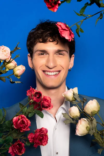 Портрет улыбающегося мужчины в элегантной одежде, смотрящего в камеру рядом с цветами на синем фоне — стоковое фото