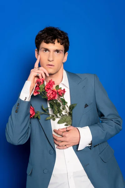 Modelo elegante na camisa e jaqueta segurando flores e posando no fundo azul — Fotografia de Stock
