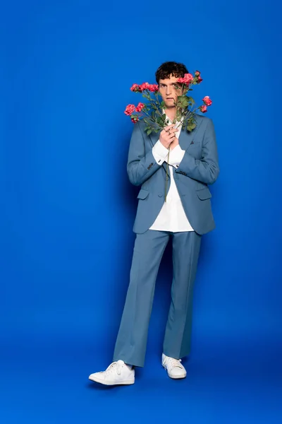 Pleine longueur de l'homme élégant en costume tenant des fleurs sur fond bleu — Photo de stock