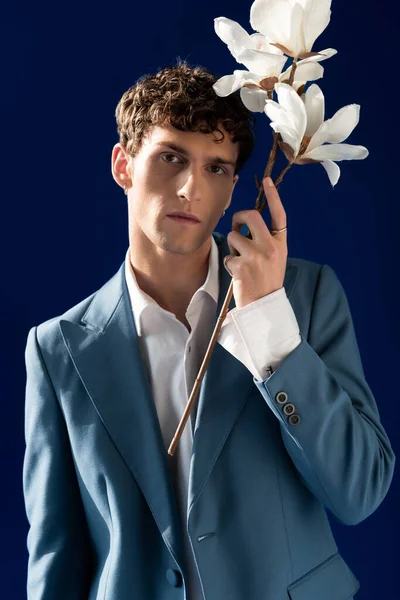 Portrait of stylish young man in jacket holding magnolia flowers isolated on navy blue — Photo de stock