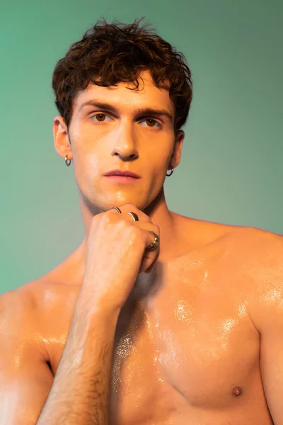Portrait of curly brunette man with oil on body looking at camera on green background — Stockfoto