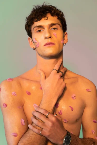 Мужчина без рубашки с лепестками на теле трогает шею на красочном фоне — стоковое фото