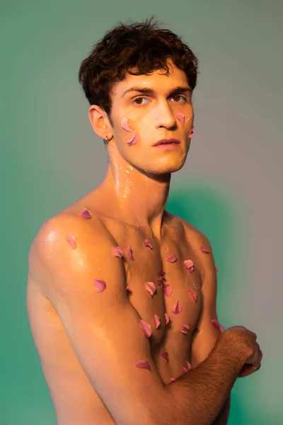 Homme sans chemise avec des pétales sur le corps et le visage sur fond coloré — Photo de stock