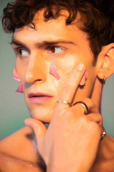 Close up view of model with floral petals on skin looking away on colorful background — Stock Photo