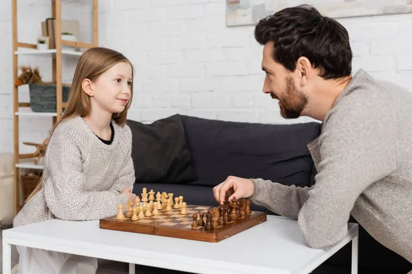 Preteen girl smiling while playing chess with bearded dad at home — Stock Photo