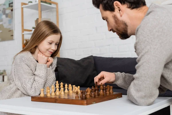Bearded man moving chess figure while playing with smiling daughter at home - foto de stock