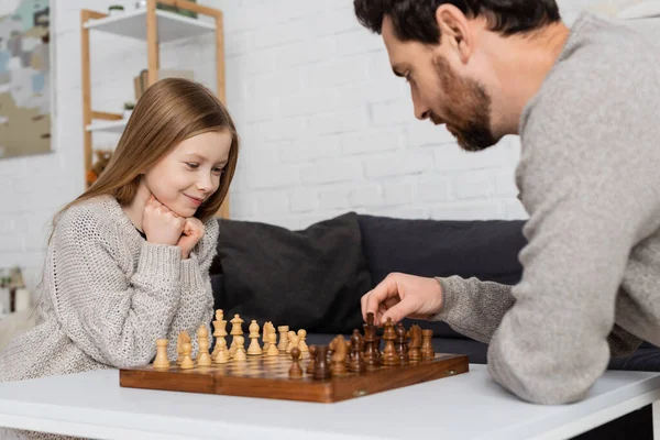 Homme barbu figurine d'échecs en mouvement tout en jouant avec fille souriante à la maison — Photo de stock