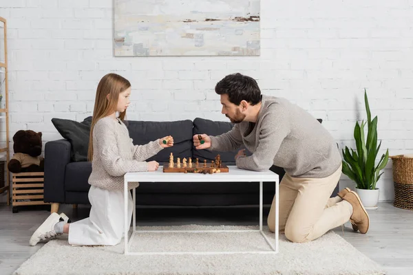 Vue latérale du père et de la fille jouant aux échecs sur la table basse dans le salon — Photo de stock