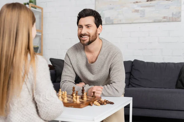 Homme barbu joyeux regardant fille floue près de l'échiquier sur la table basse — Photo de stock
