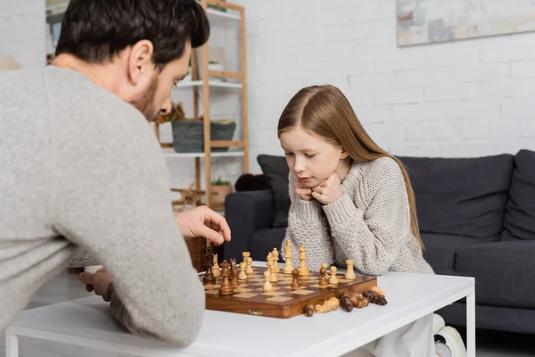 Preteen girl thinking near dad and chessboard on coffee table in living room — Stockfoto