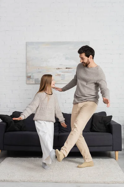 Full length of excited man with preteen daughter looking at each other while dancing in living room — Foto stock